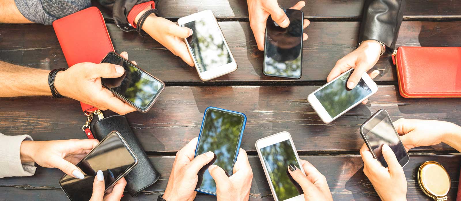 Manos de varias personas sujetando teléfonos móviles sobre una mesa al aire libre.